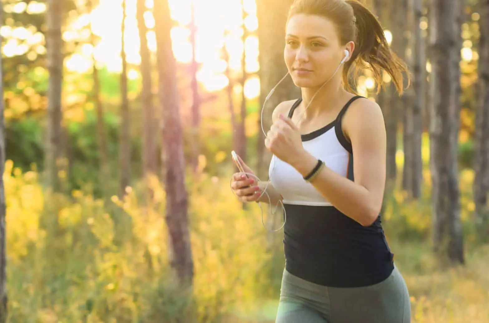 A woman jogging in the woods because she knows the importance of having a cardio exercise routine