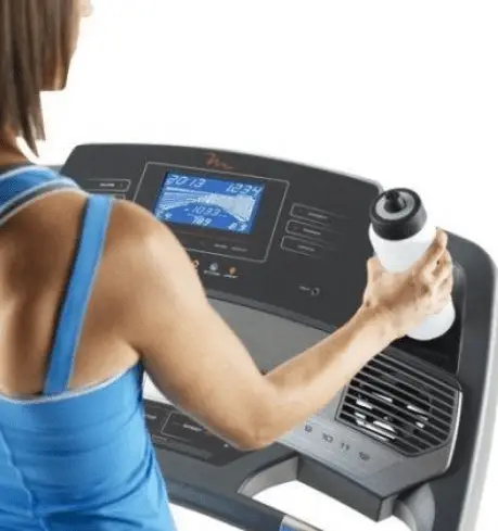 Woman wearing a blue top and putting a white water container on the Freemotion Treadmill's dashboard