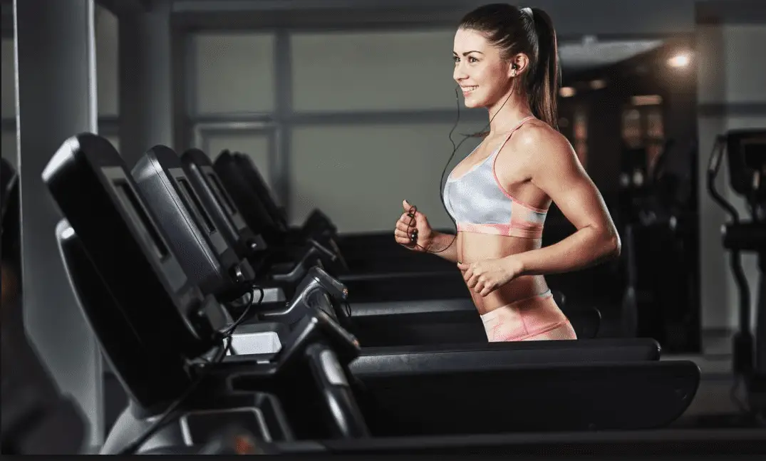 Smiling woman in sports bra running in a treadmill